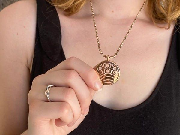 Person holding a circular pendant with spiral design on a necklace, wearing a black top.