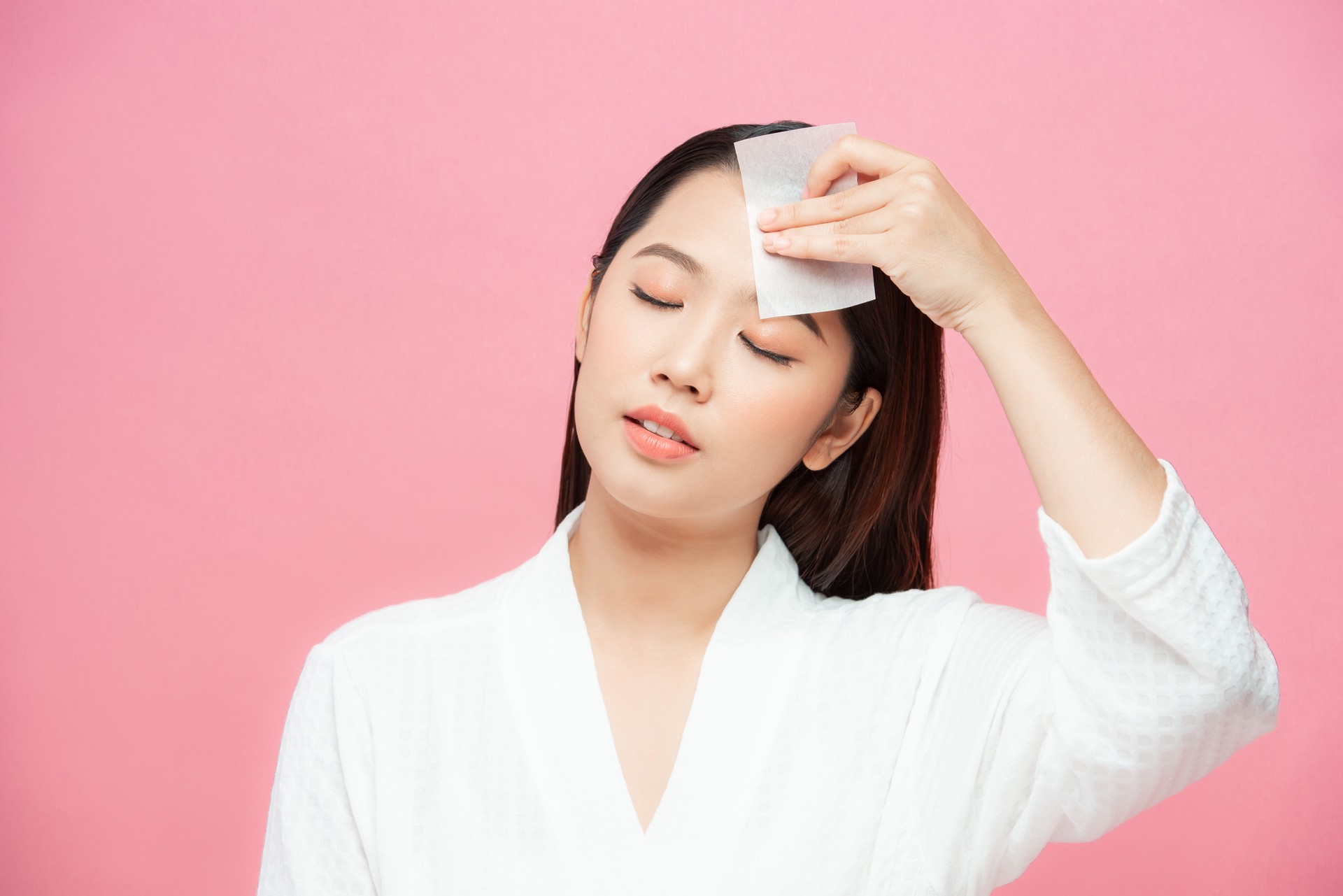 Woman using facial oil blotting paper. Photo of woman with perfect makeup on pink background. Beauty concept