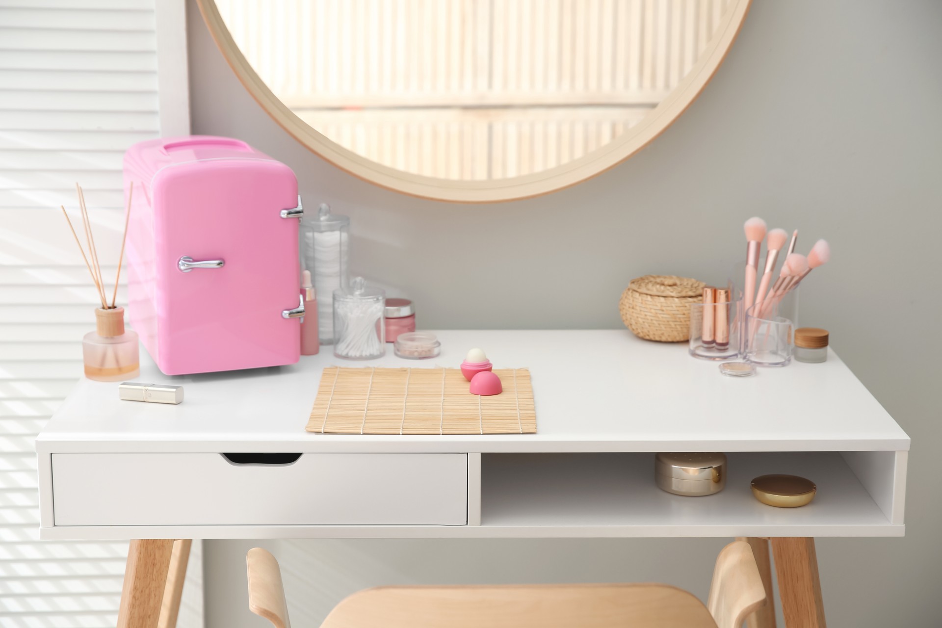 Cosmetics refrigerator and skin care products on white vanity table indoors