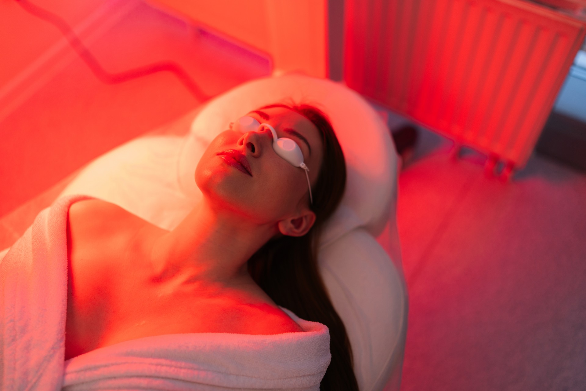 Top view face of female client lying during non-invasive type of phototherapy. Closeup of woman patient in protective goggles undergoes blue LED light therapy