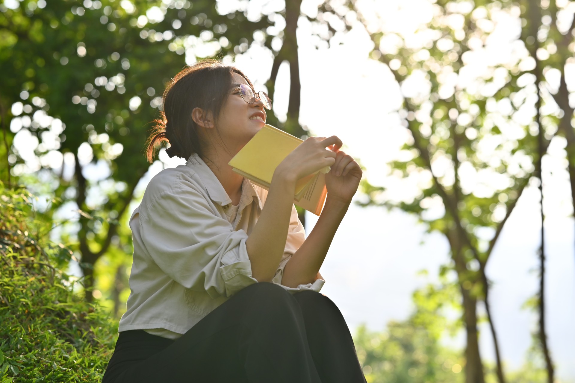 Relaxed young woman reading book on a green meadow in beautiful summer day. Education, learning and lifestyle.