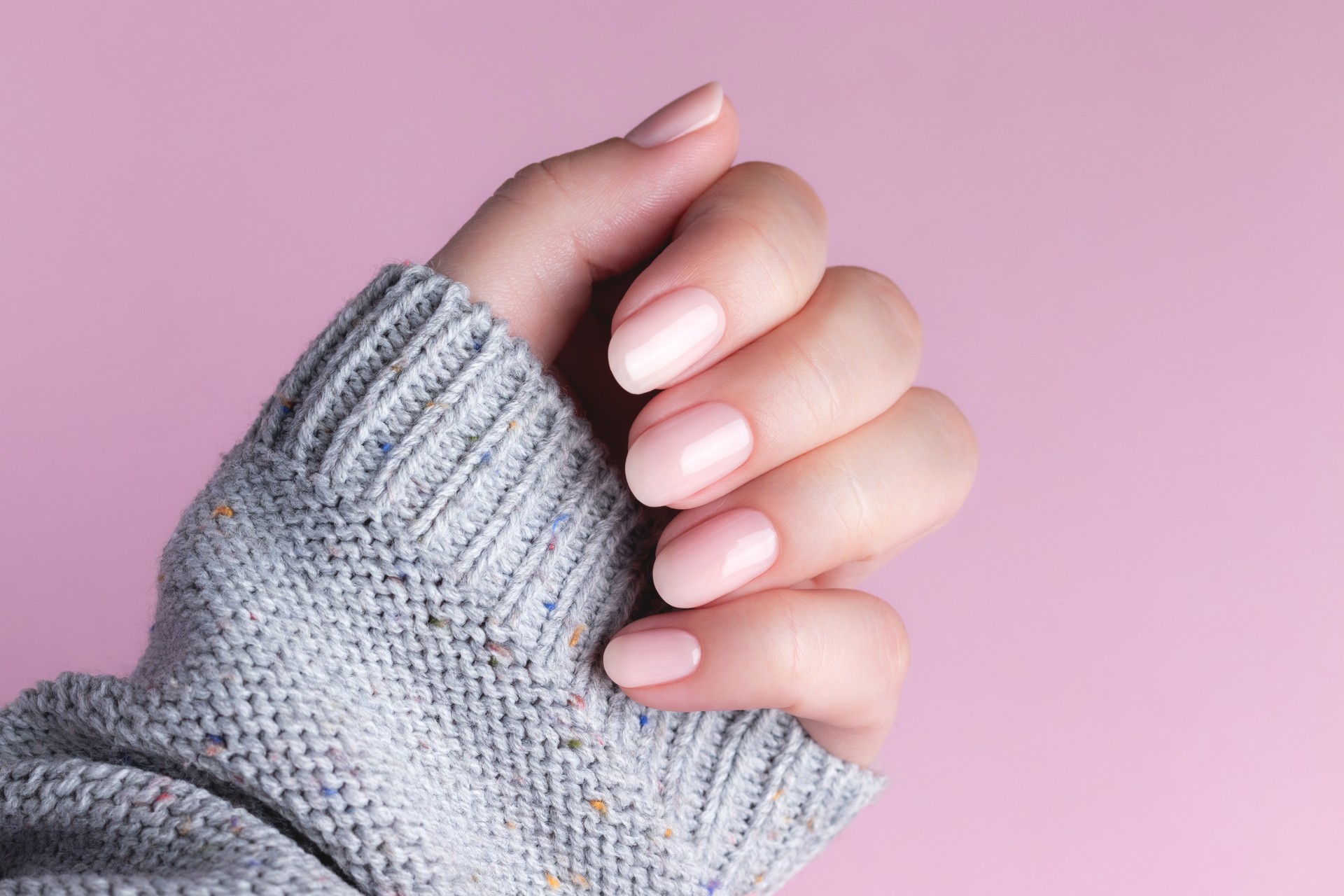 Hand in sweater with nude nails on pink background