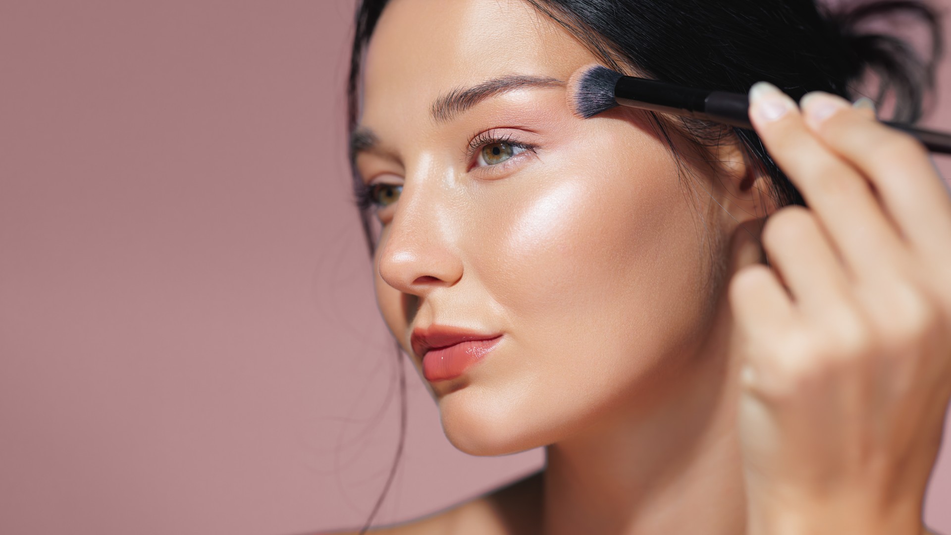 Model Applying Shimmering Highlighter on Cheekbone with Makeup Brush